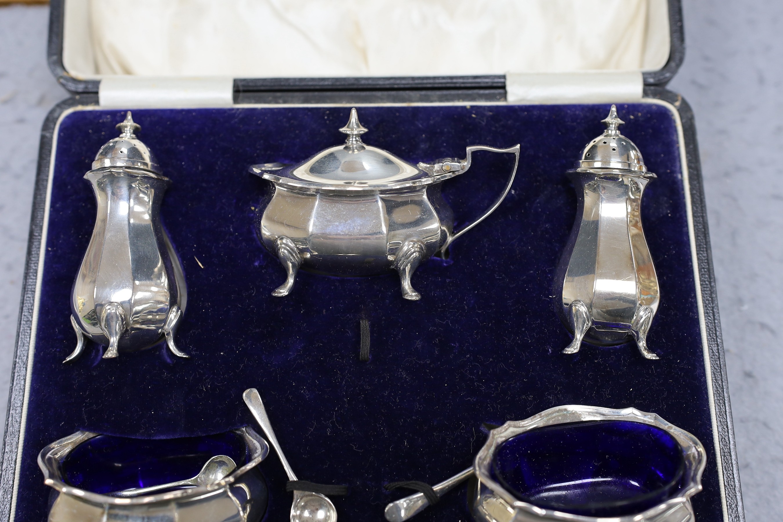 A cased George V silver five piece condiment set, Birmingham, 1921, with two associated spoons, one silver and one plated.